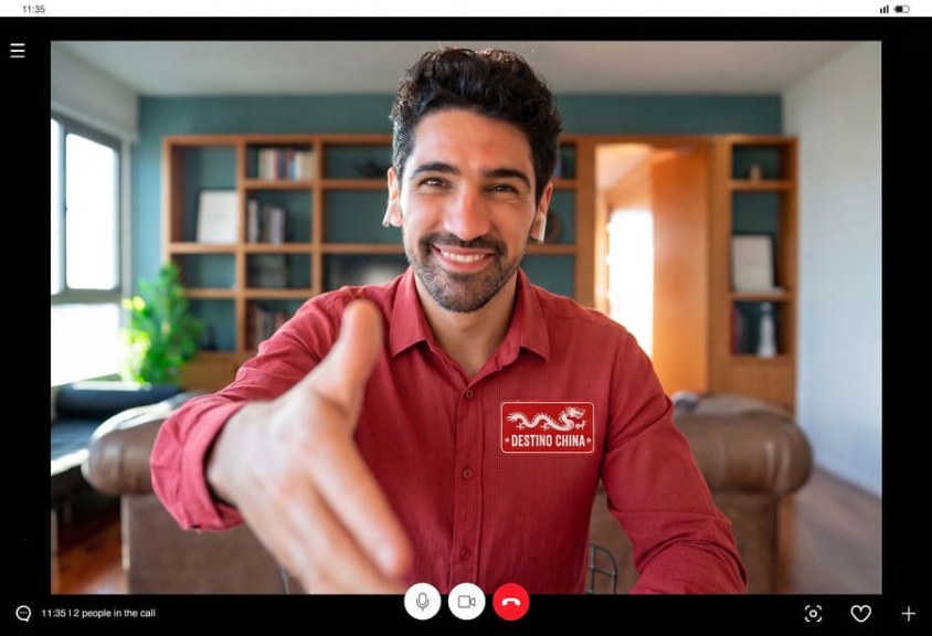 Asesor de viajes de Destino China sonriente realizando una videollamada y extendiendo la mano en señal de bienvenida para planificar aventuras auténticas.